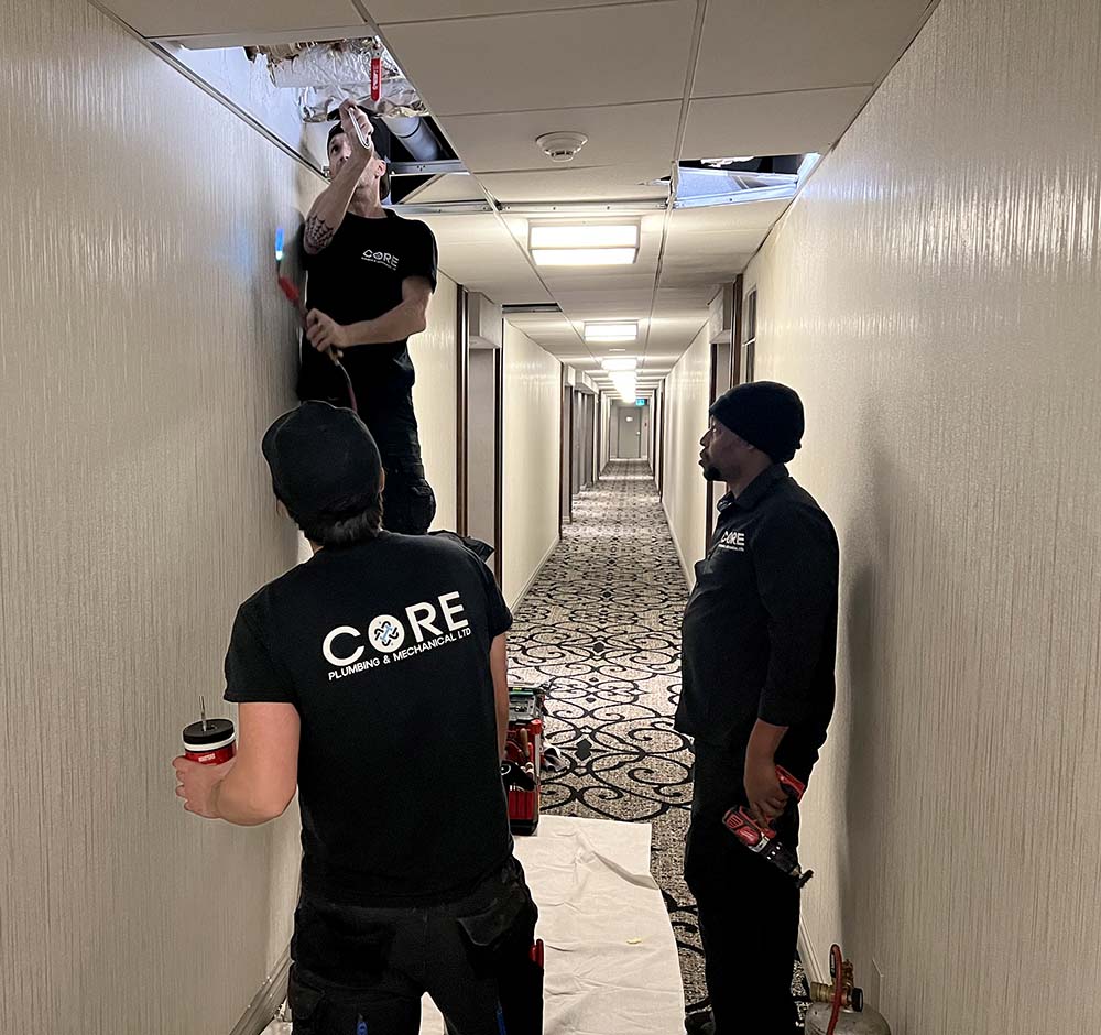 Core Plumbing team in action: Three employees replacing a riser valve, one using a torch behind a removed ceiling tile.