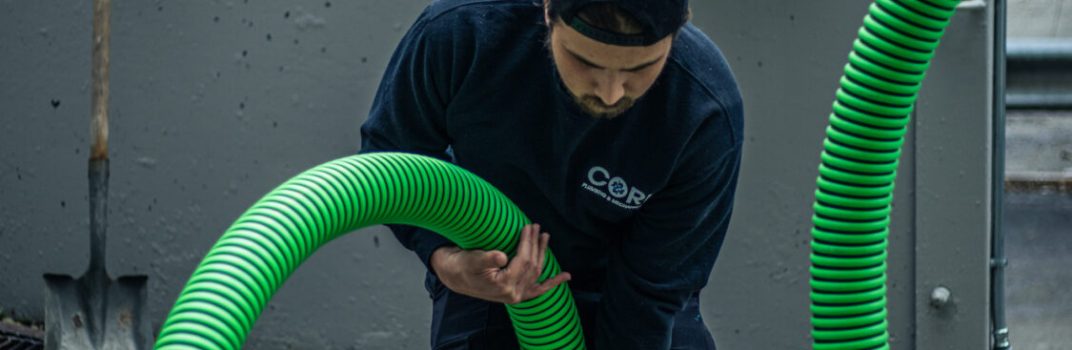 Core Plumbing employee using a vacuum to clean a trench drain, ensuring optimal drainage performance.
