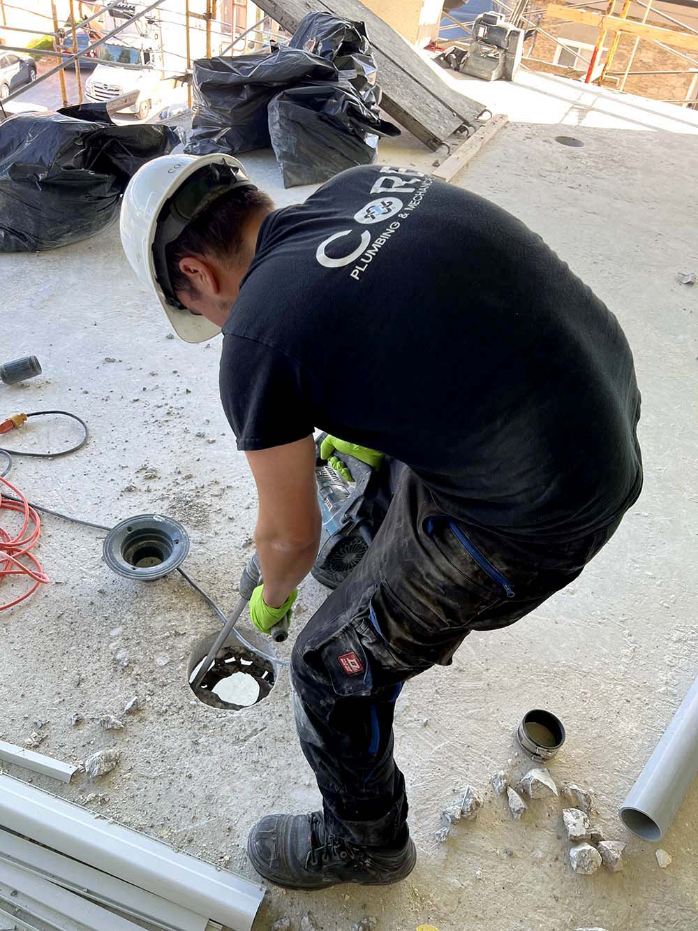 Core Plumbing employee skillfully chipping out a hole in a concrete slab for the installation of an area drain.